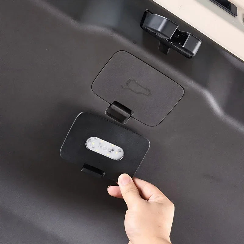 Hand opening a black matte plastic storage compartment with integrated LED lighting in a car.