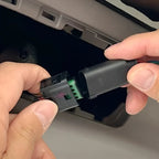 Hands connecting a black electrical wiring harness connector inside a vehicle interior.
