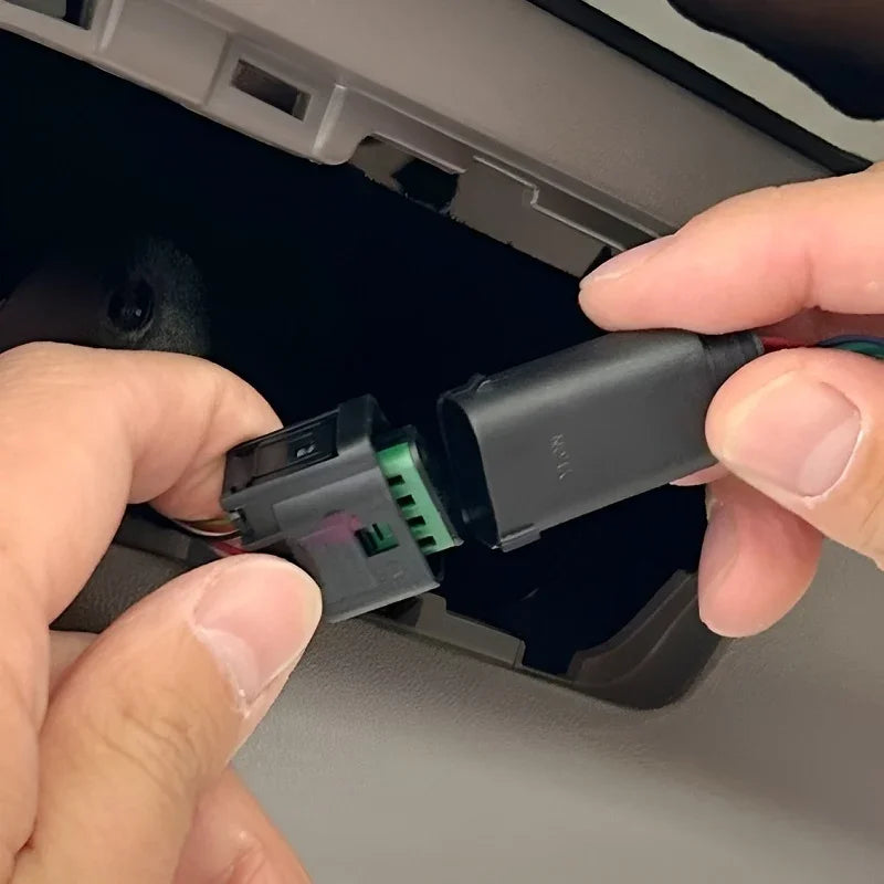 Hands connecting a black electrical wiring harness connector inside a vehicle interior.