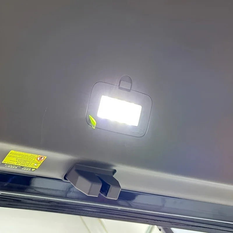 Interior view of a black car ceiling featuring a bright LED reading light and a safety warning label.