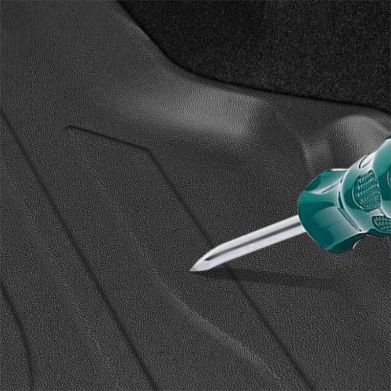 Durable black textured rubber car floor mat being tested for scratch resistance with a screwdriver.