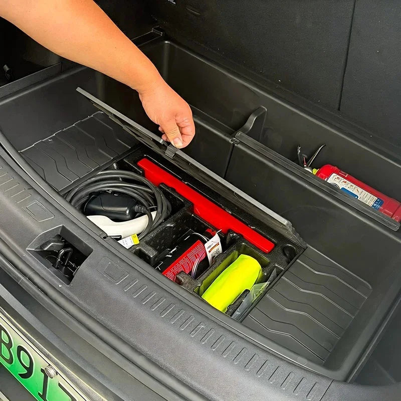 A person organizing a black trunk organizer with a red tool kit and various accessories in a car trunk.