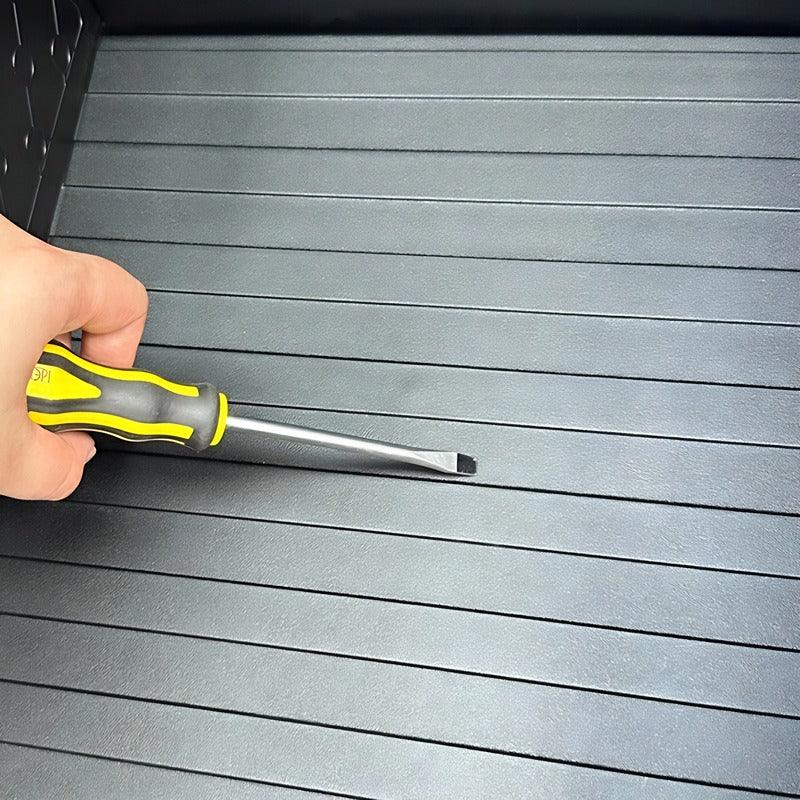 Black textured rubber car trunk mat being fitted with a yellow and black precision tool.