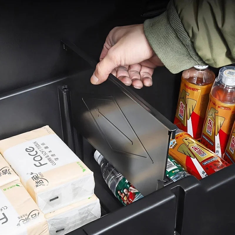 Black matte car organizer compartment with a sliding lid storing beverages and tissues.