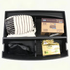 Black plastic car organizer tray containing a striped cushion, a cardboard box, and packaged goods.