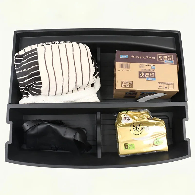 Black plastic car organizer tray containing a striped cushion, a cardboard box, and packaged goods.