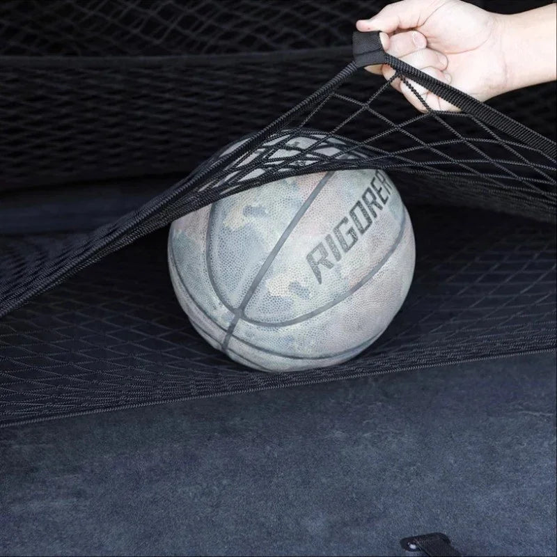 Black elastic mesh cargo net securing a basketball in a car trunk.