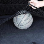 Black elastic mesh cargo net securing a basketball in a car trunk.