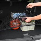 Black mesh cargo net securing a basketball and storage box in a car trunk.