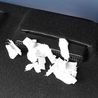 Black textured car trash bin with white paper waste on dark carpet floor.