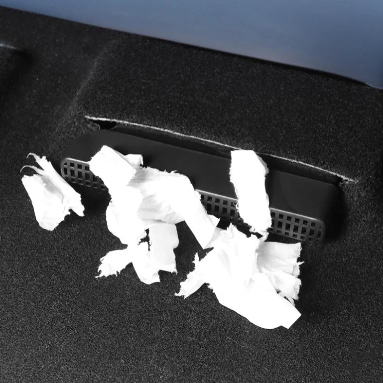 Black textured car trash bin with white paper waste on dark carpet floor.
