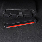 Black plastic car interior trim piece with a red adhesive strip on a dark carpet surface.