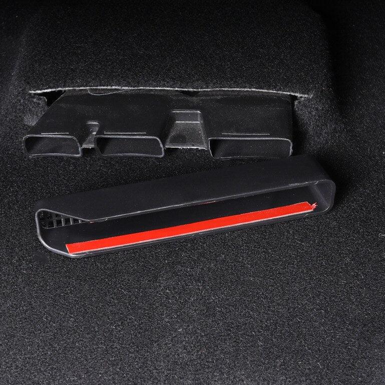 Black plastic car interior trim piece with a red adhesive strip on a dark carpet surface.