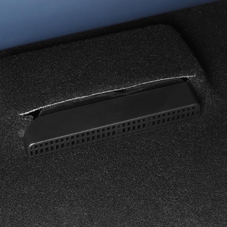 Close-up of a black perforated plastic vent integrated into a grey carpeted car interior.