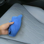 A hand cleaning grey perforated leather car seat covers with a blue microfiber cloth.