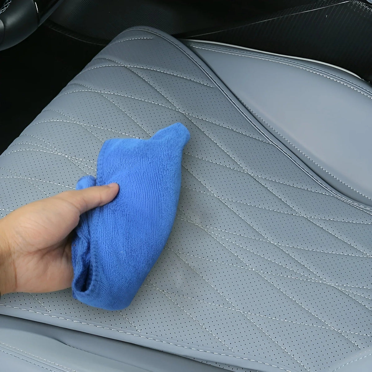 A hand cleaning grey perforated leather car seat covers with a blue microfiber cloth.