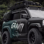 Black off-road SUV with 'GRAVITY' decal, roof rack, storage boxes, and rugged tires.