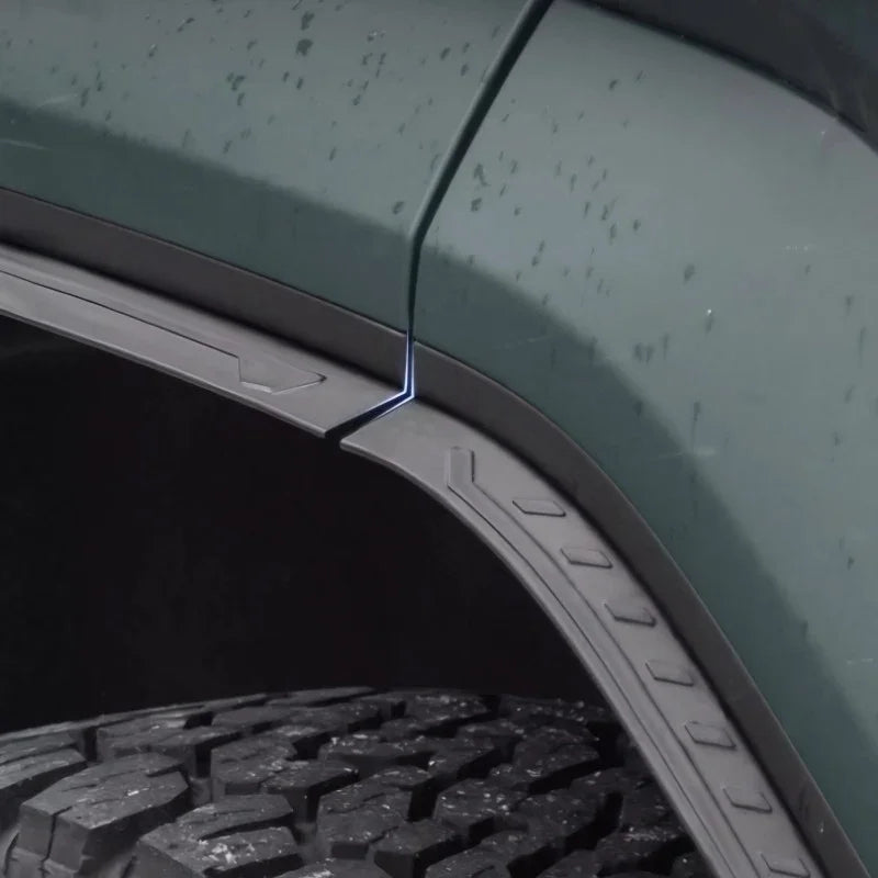 Durable matte black textured fender flares installed on a dark green vehicle wheel arch.