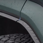 Durable matte black textured fender flares installed on a dark green vehicle wheel arch.