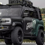 Matte black and dark green rugged off-road SUV featuring heavy-duty roof racks and all-terrain tires.