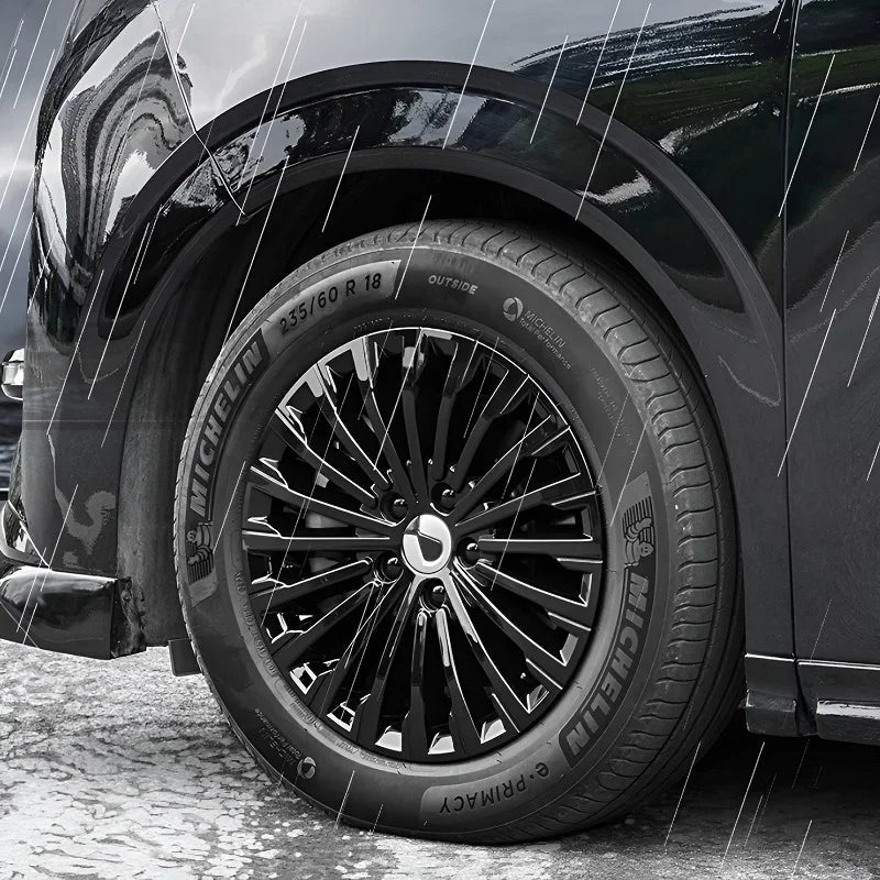 Close-up of a black Michelin Primacy tire on a multi-spoke black rim of a black car in the rain.
