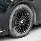 Close-up of a black Michelin Primacy tire mounted on a multi-spoke black alloy rim of a dark vehicle.