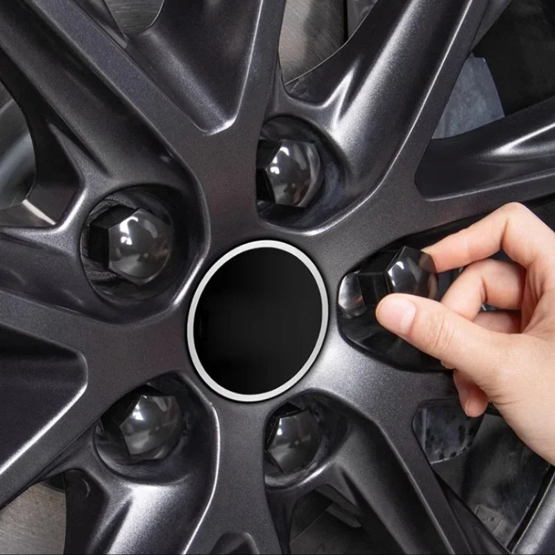 Hand installing a black matte lug nut cover onto a dark grey metallic car wheel rim.