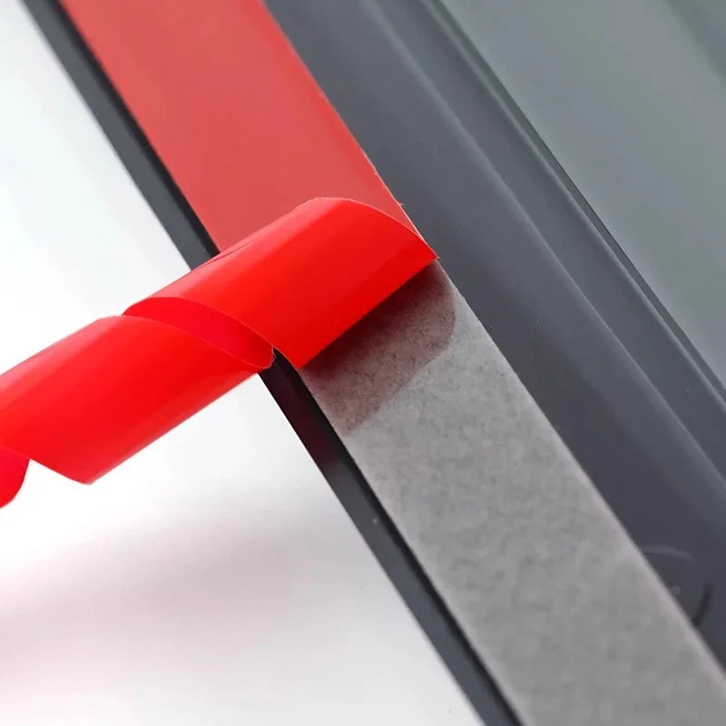 Close-up of a grey weatherstrip seal with a red adhesive backing being peeled away.