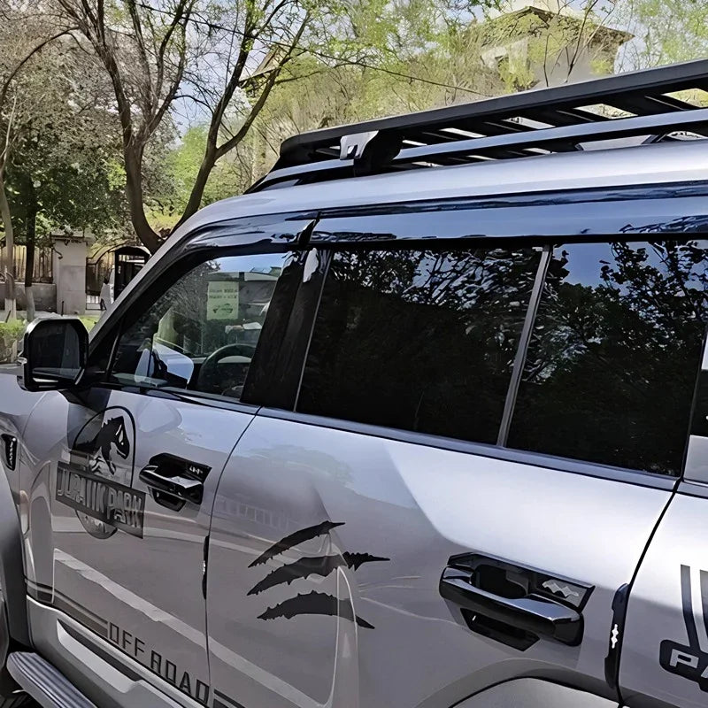 Silver BYD off-road vehicle featuring black Jurassic Park claw decals and a sleek roof rack.
