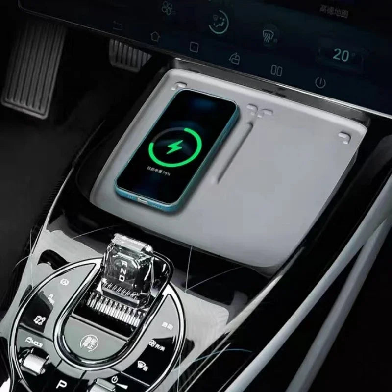 Light gray wireless charging pad with a blue smartphone charging in a BYD car interior.