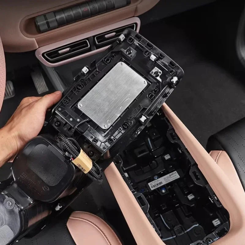Black plastic central console component with silver metallic plate being installed in a car interior.