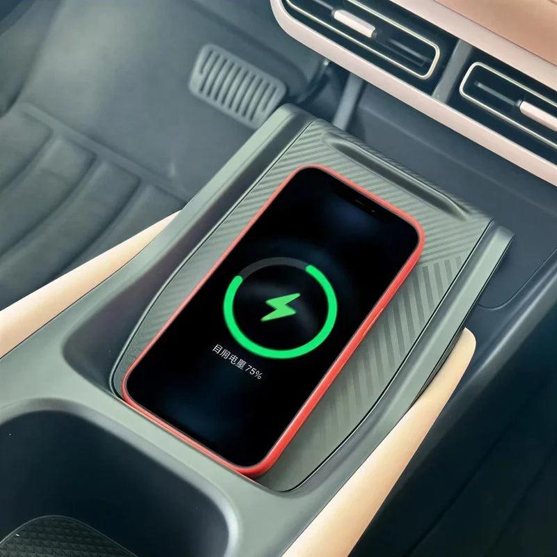 Red-edged smartphone charging on a black carbon fiber texture wireless charging pad in a car.